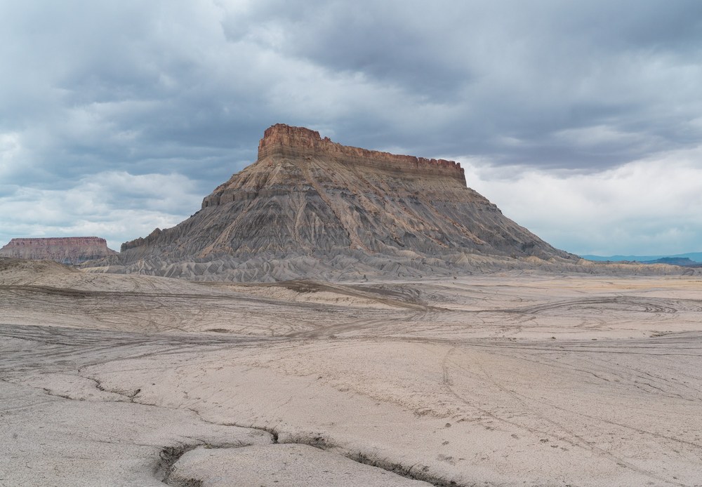 Factory Butte rises above an expansive gray desert landscape in Utah.