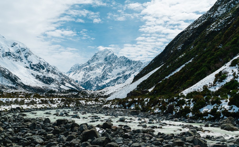 Snow-covered peaks frame a rocky riverbed in Aoraki/Mount Cook National Park, New Zealand.